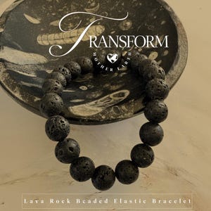 May include: A black lava rock beaded elastic bracelet. The bracelet is made of round, porous lava rock beads. The bracelet is displayed on a decorative, dark-colored bowl. The text "TRANSFORM" and "Mother Earth" are visible in the image.