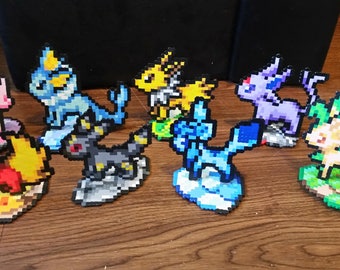 May include: A collection of pixel art figures of various colorful creatures. The figures are in different poses and colors, including red, yellow, blue, purple, and green. They are arranged on a wooden surface.
