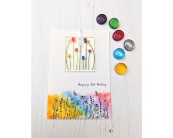 Op de afbeelding: Een witte kaart met een regenboog waterverf achtergrond en een zwarte lijntekening van bloemen. De kaart heeft een vierkant glazen paneel met kleurrijke glazen bloemen en de tekst "Happy Birthday".