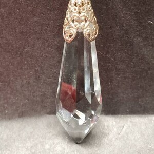 May include: A clear crystal teardrop pendant with a gold filigree top and a string of purple beads.