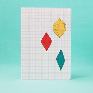 Könnte beinhalten: Ein weißes Notizbuch mit einem Gittermuster und drei bunten geometrischen Formen, die darauf gezeichnet sind. Die Formen sind eine rote Raute, eine gelbe Raute und eine blaue Raute.
