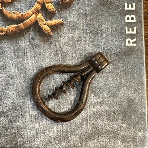 May include: A vintage metal corkscrew with a  spiral design. The corkscrew is in the shape of a teardrop and has a dark brown patina.