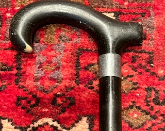 May include: A black wooden walking stick with a curved handle and a silver band.