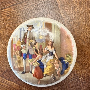 May include: A vintage ceramic plate with a colorful illustration of people selling goods in a street scene. The plate features the text "Cries of London - Primroses - Yellow Primroses".