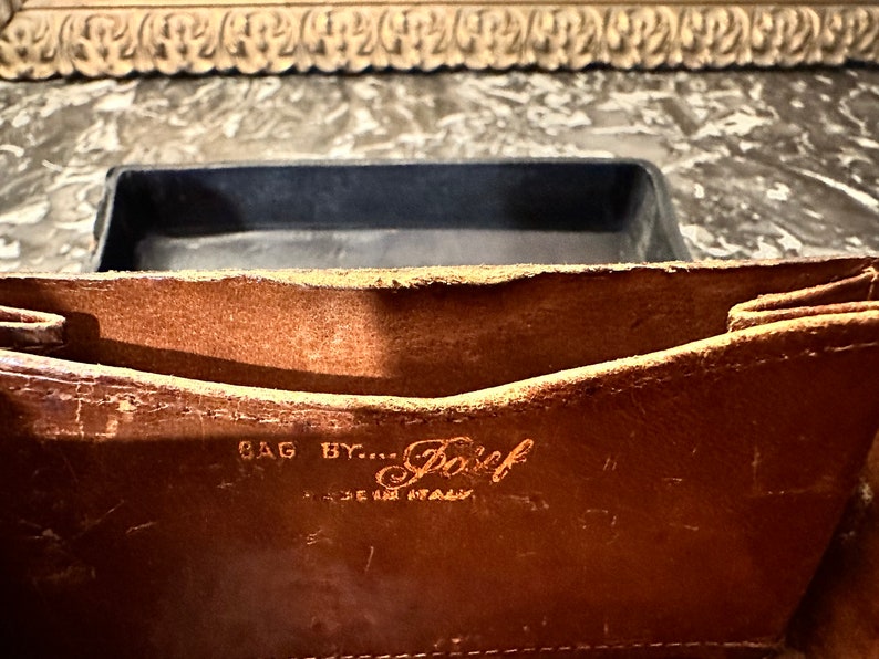 Puede incluir: Primer plano del interior de un bolso de cuero marr&oacute;n. El texto "BAG BY... Posef MADE IN ITALY" es visible. El bolso tiene un aspecto desgastado y vintage, con desgaste visible en el cuero.