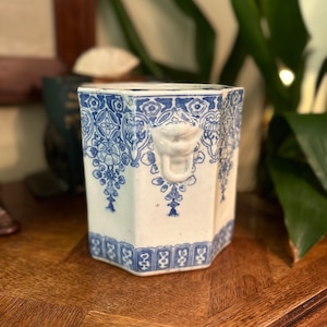 May include: A white ceramic octagonal vase with a blue and white floral pattern. The vase has a lion's head handle.