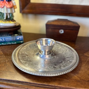 May include: A silver serving dish with an ornate design and a small, silver bowl in the center. The dish has a raised edge and a beaded border.