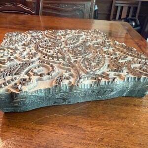 May include: A rectangular, dark-colored wooden block with an intricate, carved paisley design. The block's surface features a detailed pattern of swirling shapes and floral elements, perfect for textile printing or decorative purposes.