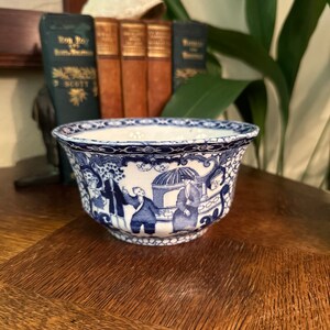 May include: A blue and white porcelain bowl with a floral design and a scalloped rim. The bowl is decorated with a scene of people in a garden.