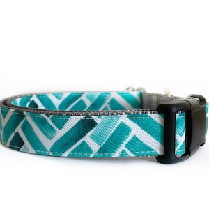 Op de afbeelding: Een turquoise en wit gepatroneerde hondenriem met een zwarte plastic gesp. De riem is gemaakt van duurzaam webbing en heeft een grijze afwerking.