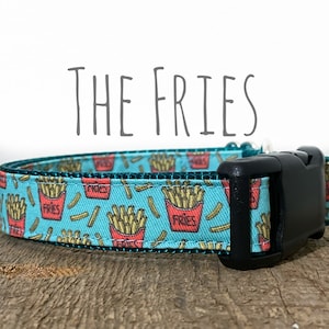 Peut inclure: Un collier pour chien bleu turquoise avec une boucle noire. Le collier a un motif répété de frites rouges et jaunes sur un fond bleu. Le texte "FRIES" est imprimé sur les boîtes rouges.