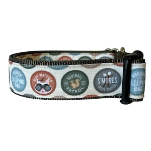 Puede incluir: Un collar de perro blanco y marrón con un patrón verde, azul y naranja. El collar presenta cinco parches circulares con texto e imágenes, incluyendo "Squirrel Patrol", "Bird Watcher", "S'mores Taste Tester", "Hogged the Sleeping Bag" y "Hogged the Sleeping Bag".