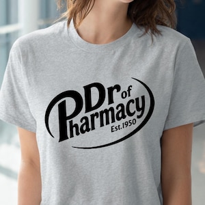 May include: A light gray t-shirt with the text "Dr of Pharmacy Est. 1950" in a black, stylized design. The shirt is short-sleeved and has a crew neck.