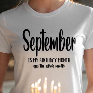 May include: White t-shirt with the text "September is MY BIRTHDAY MONTH *yes the whole month*". The shirt is being held over a birthday cake with lit candles. The text is in a black, cursive font.