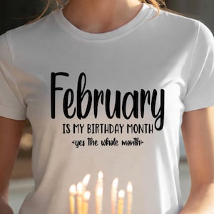May include: White t-shirt with the text "February is my birthday month - yes the whole month" in black script. The person is holding a birthday cake with lit candles. The shirt is a crew neck.