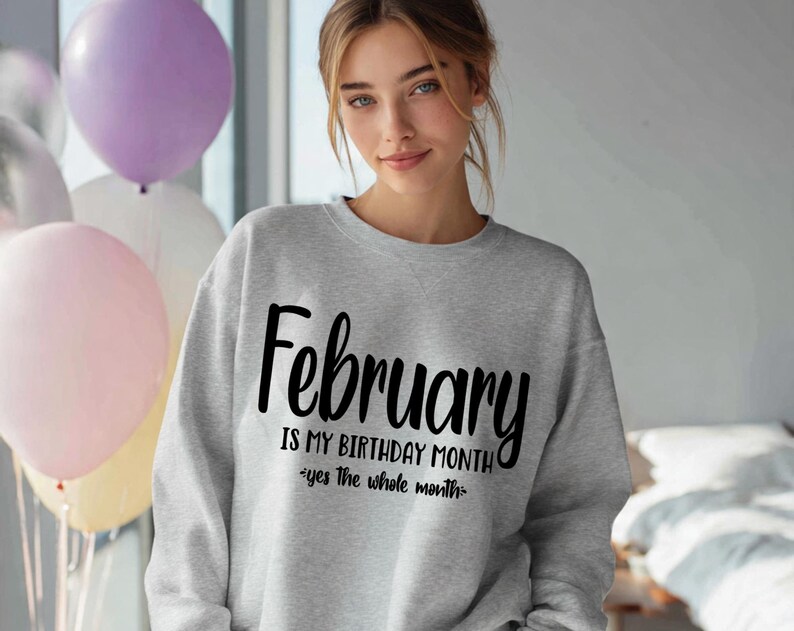 May include: A light gray sweatshirt with the word "February" in large black script. Below, the text reads "IS MY BIRTHDAY MONTH" and "yes the whole month" in a smaller font. The image includes balloons in the background.