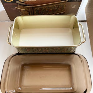 May include: A Pyrex Originals Fireside Bakeware set with a brown glass loaf pan and a metal roasting pan with a floral design. The box reads "The gleam of brass, the glow of Fireside Bakeware. An elegant accent for the table or buffet."