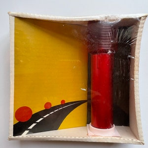 May include: A vintage boxed set featuring a red, cylindrical object and a yellow and black graphic. The graphic depicts a road with red circles. The set is encased in clear plastic wrap and a cardboard box.
