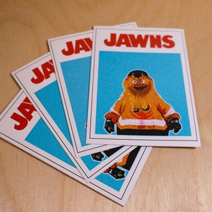 An array of 4 (four) stickers that look like the famous JAWS movie poster but feature a cartoon image of NHL Philadelphia Flyers mascot Gritty.