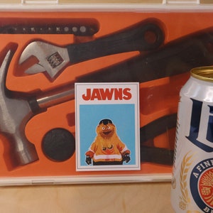 Photo of an orange Ikea tool set, with a Gritty sticker that looks like the JAWS movie poster, but says JAWNS. There is a miller lite beer can in the foreground right corner.