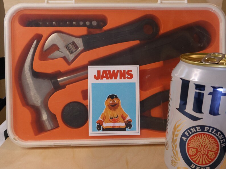 Photo of an orange Ikea tool set, with a Gritty sticker that looks like the JAWS movie poster, but says JAWNS. There is a miller lite beer can in the foreground right corner.