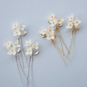 May include: Set of six hair pins with white felt flower accents. Three pins have gold wire stems and leaves, and three pins have silver wire stems and leaves.