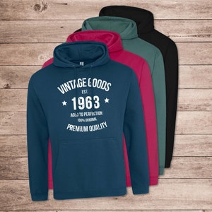 May include: A blue hooded sweatshirt with white text that reads "Vintage Goods Est. 1963 Aged to Perfection 100% Original Premium Quality". The sweatshirt is shown with other hooded sweatshirts in black, teal, and pink.