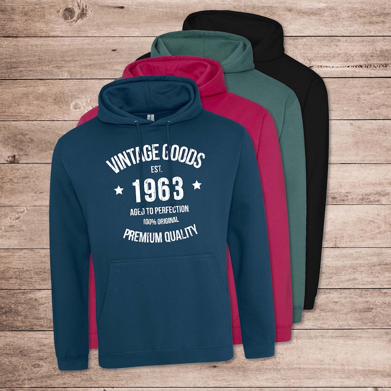 May include: A blue hooded sweatshirt with white text that reads "Vintage Goods Est. 1963 Aged to Perfection 100% Original Premium Quality". The sweatshirt is shown with other hooded sweatshirts in black, teal, and pink.