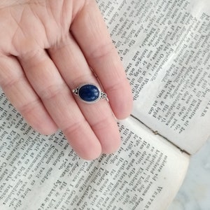 May include: A silver ring with a dark blue oval gemstone. The ring is set on a finger.
