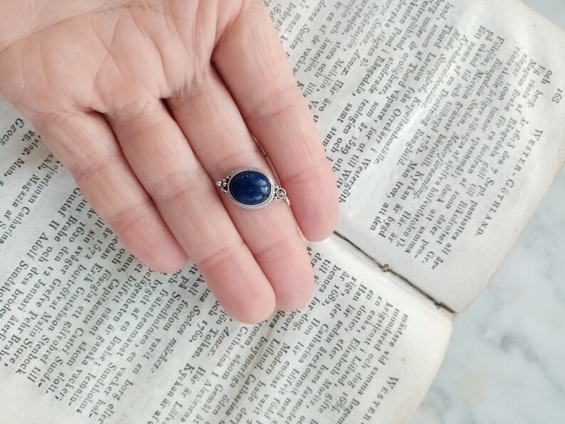 May include: A silver ring with a dark blue oval gemstone. The ring is set on a finger.