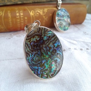 May include: Two silver oval pendants with iridescent abalone shell inlays. The shell has a blue, green, and brown colour pattern.