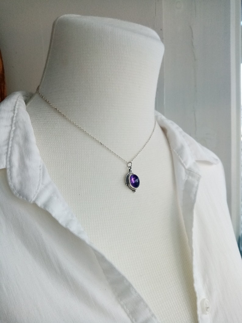 May include: A silver chain necklace with a pendant featuring a purple gemstone set in a silver bezel.