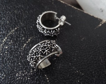 May include: A pair of silver hoop earrings with a delicate floral design. The earrings are made of metal and have a polished finish.