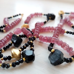 May include: A multi-strand necklace with pink and black beads. The necklace features gold accents and large black gemstone beads.