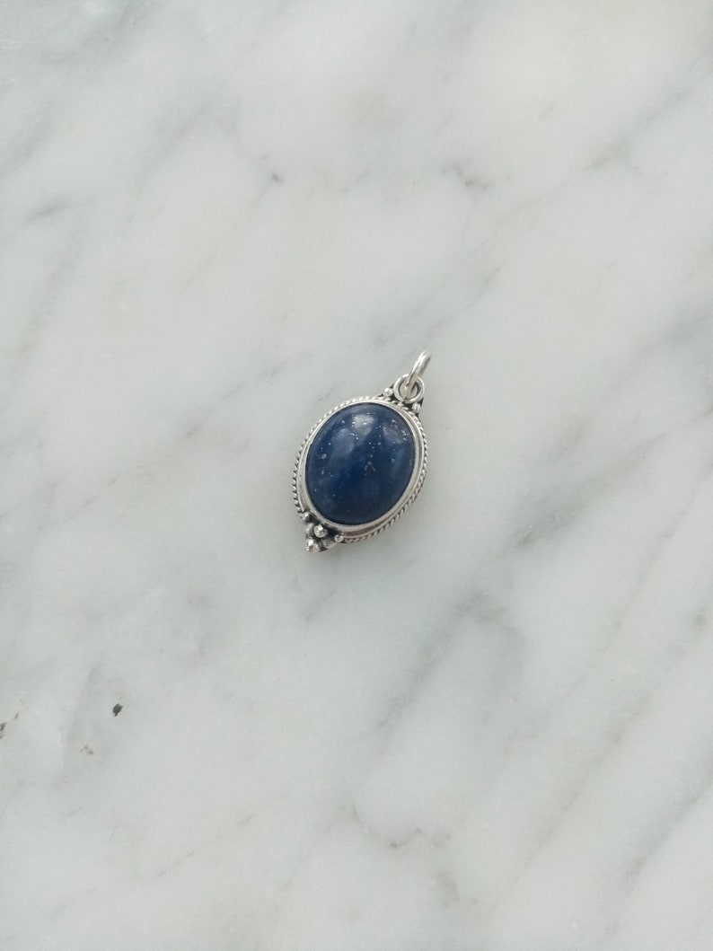 May include: A silver pendant with a dark blue oval gemstone set in a silver frame.