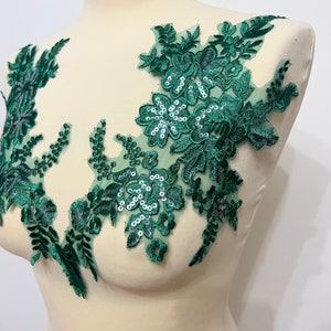 Könnte beinhalten: Grüne florale Spitzenapplikation mit Pailletten. Die Applikation zeigt ein zartes Blumenmuster mit grünen Samtblättern und silbernen Pailletten.