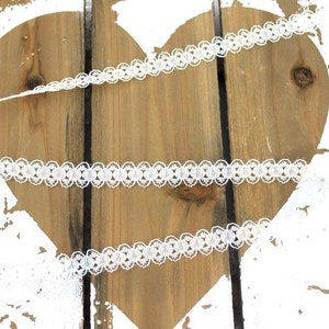 May include: White lace trim with a delicate floral pattern. The lace is shown on a wooden heart background.