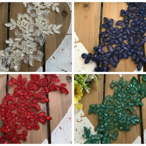 Könnte beinhalten: Vier florale Spitzenapplikationen mit Pailletten in verschiedenen Farben: Elfenbein, Marineblau, Rot und Grün. Die Applikationen befinden sich auf einem Holzgrund.