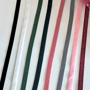 Könnte beinhalten: Sortiment aus zehn verschiedenen farbigen Bandbesätzen. Die Bänder sind alle aus Samt und in Schwarz, Weiß, Dunkelgrün, Dunkelblau, Rosa, Grau und Hellrosa erhältlich.