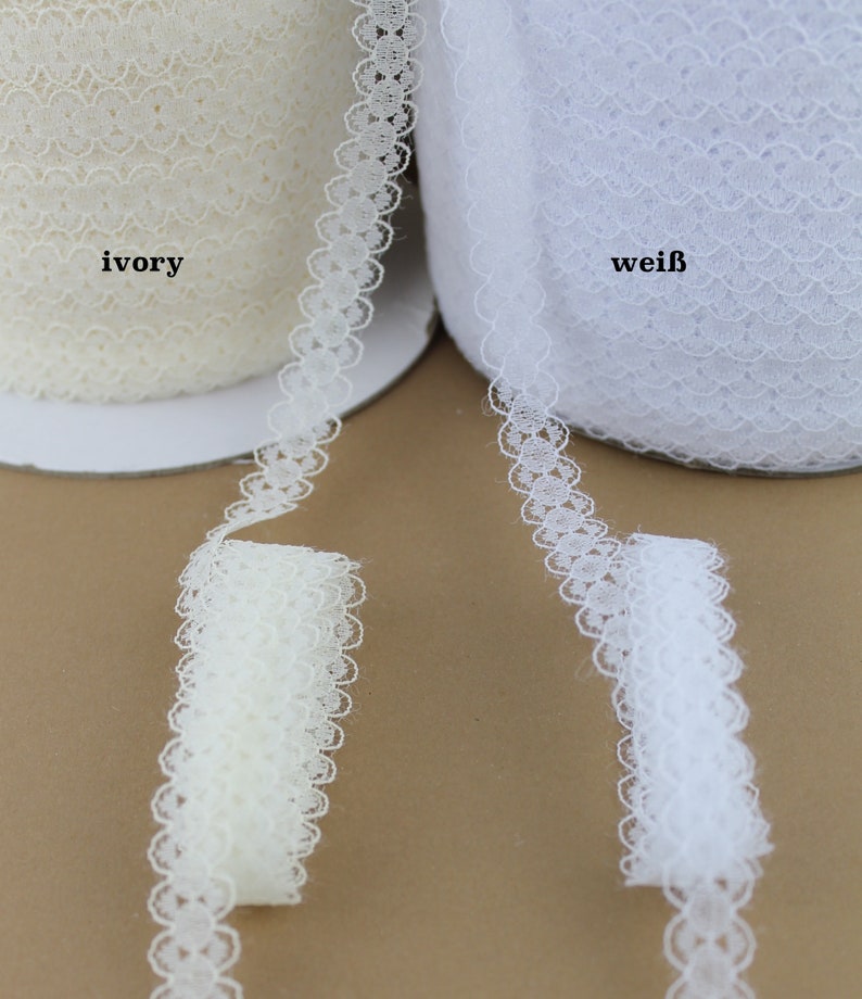 May include: Two spools of white lace trim, one ivory and one white. The lace trim has a scalloped edge with a delicate floral pattern.