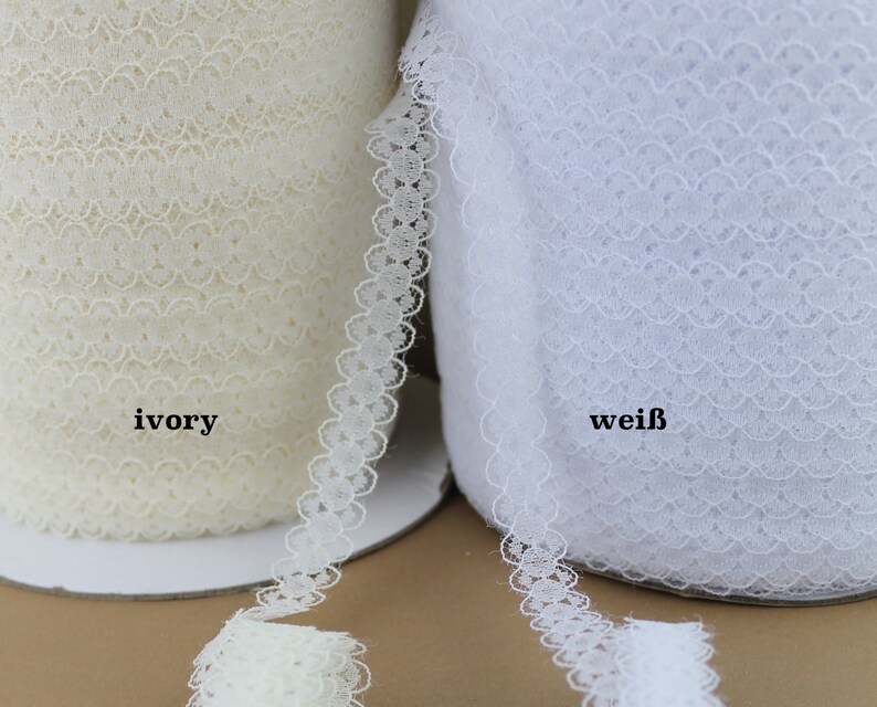 May include: Two spools of white lace trim, one ivory and one white. The lace has a delicate scalloped edge.