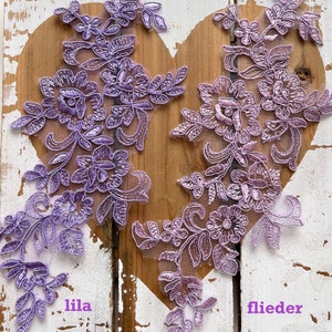 May include: Two pieces of purple lace trim with floral designs. The trim on the left is labelled "lila" and the trim on the right is labelled "flieder".