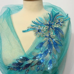 Könnte beinhalten: Ein türkisfarbener Tüllstoff mit einer blauen und goldenen Blumenapplikation. Die Applikation ist mit Pailletten und Stickereien verziert.