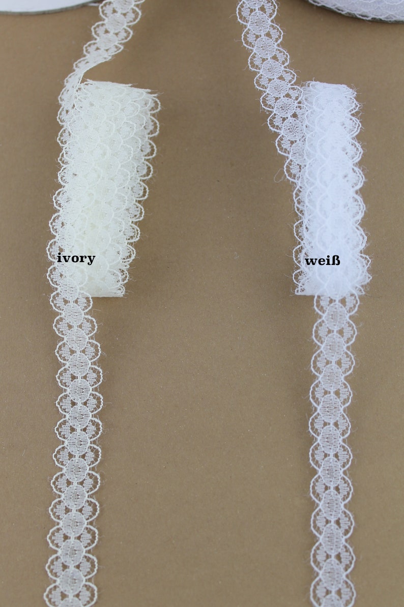 May include: Two spools of white lace trim, one ivory and one white. The lace has a scalloped edge with small circles.