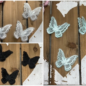 Op de afbeelding: Assortiment van vlinderapplicaties in wit, zwart en lichtblauw. De applicaties zijn gemaakt van kant en zijn perfect om een vleugje whimsy toe te voegen aan elk project.