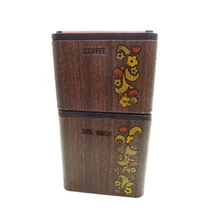 May include: A rectangular, two-tiered storage container with a dark brown wood grain finish. The top section is labeled COFFEE and the bottom section is labeled TEA BAGS. Both sections feature a vertical floral pattern in yellow and orange.