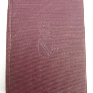 May include: A maroon-colored book with a textured cover. The cover features an embossed emblem of a bear above a shield. The book is closed and appears to be in good condition. The spine is visible on the left side.