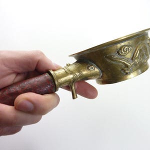 May include: An antique brass incense burner with a detailed dragon design on the bowl. The handle is wrapped in a reddish-brown material. The burner is held against a white background.