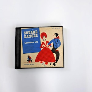 May include: Vintage vinyl record album titled "Square Dances" by Lawrence Loy. The album cover features a blue and beige design with illustrations of dancing figures in red, blue, and black. The album is in a black case.