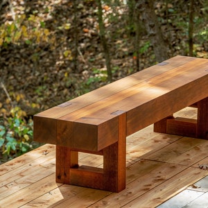 May include: A rustic wooden bench with a natural wood finish. The bench has a simple design with a rectangular seat and square legs. The bench is made of solid wood and has a natural wood grain.